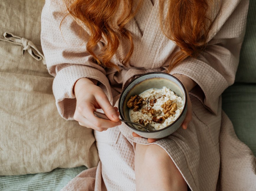 an overhead photo of a person wearing a rob holding a bowl of cereal sitting on the couch while sick