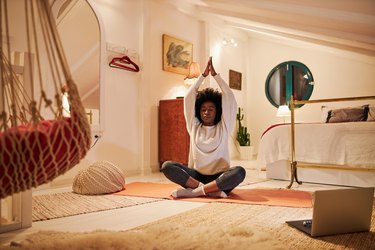 Young person with afro doing yoga stretched for lupus before bed in a cozy bedroom