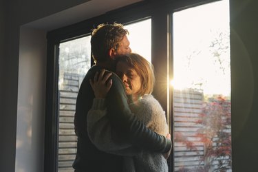 Close up shot of a couple standing in front of a window holding each other in a tight hug, as an example of how to help someone with depression