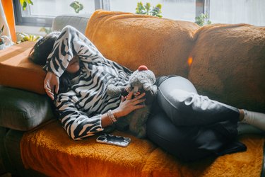 a person wearing a zebra-patterned sweater lying on an orange couch with their arm over their face and their other hand on their stomach because they have food poisoning or the stomach flu